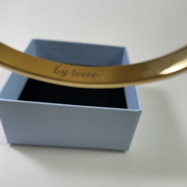 A gold bracelet is in the box and has a message written on it.