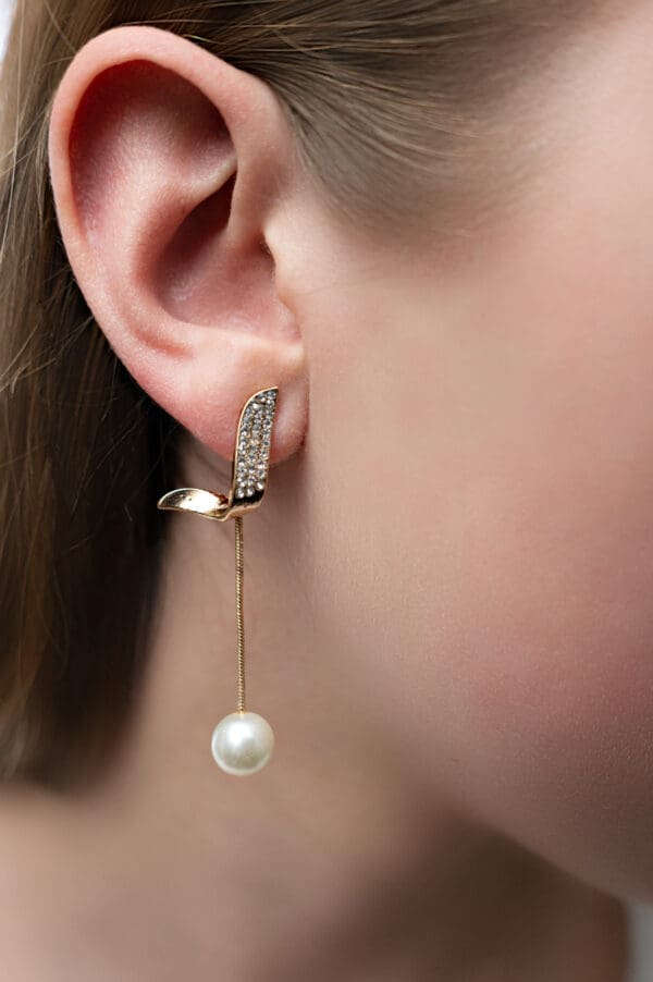 A woman wearing earrings with pearls hanging from them.