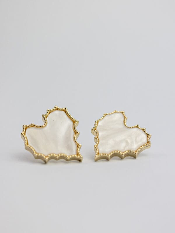 A pair of gold and white earrings on a table.