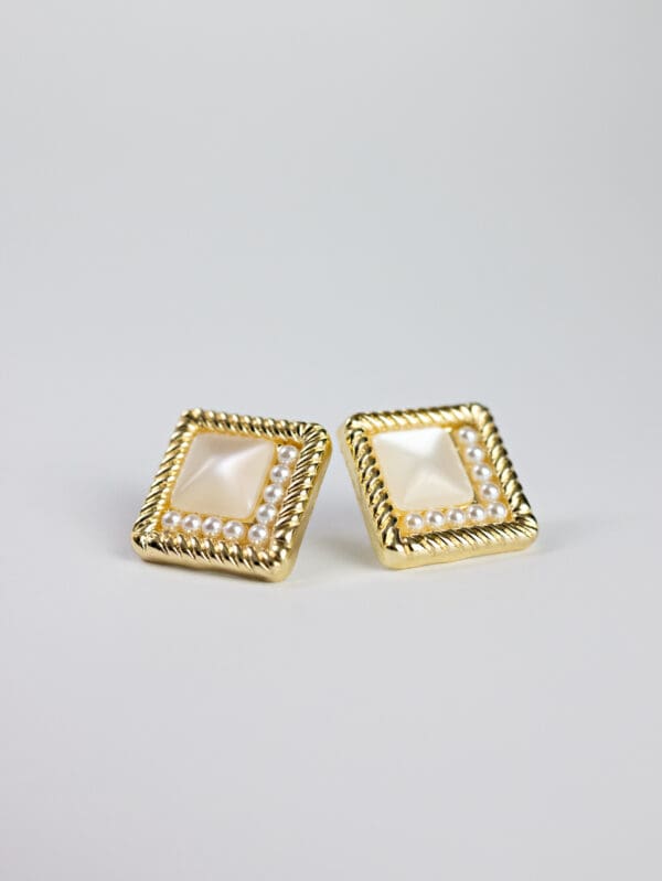 A pair of gold earrings with pearls on top.